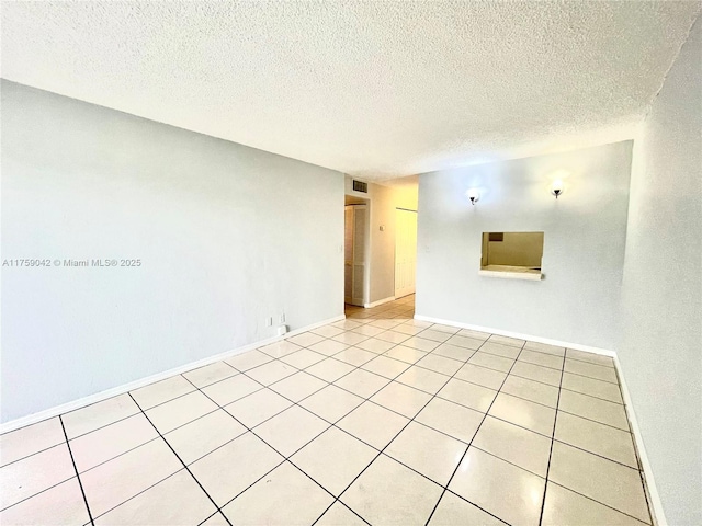 empty room with light tile patterned floors, baseboards, visible vents, and a textured ceiling