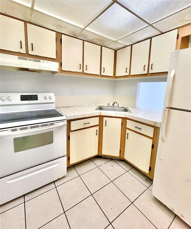 kitchen with under cabinet range hood, a sink, white appliances, light tile patterned floors, and a paneled ceiling