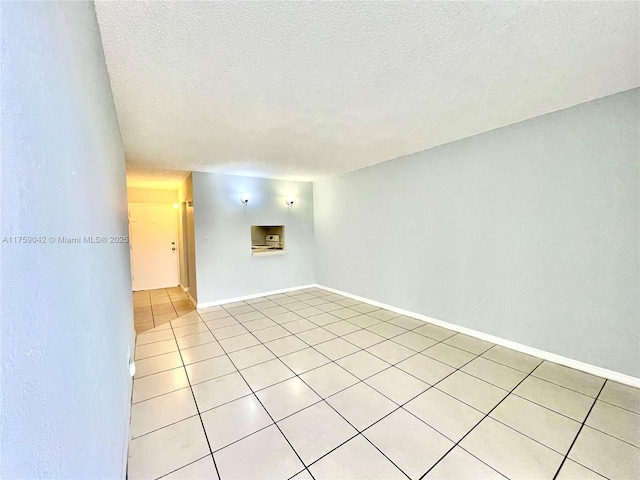 empty room featuring light tile patterned floors, a textured ceiling, and baseboards