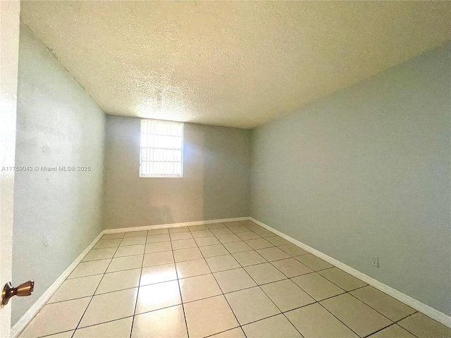 unfurnished room with light tile patterned flooring, a textured ceiling, and baseboards