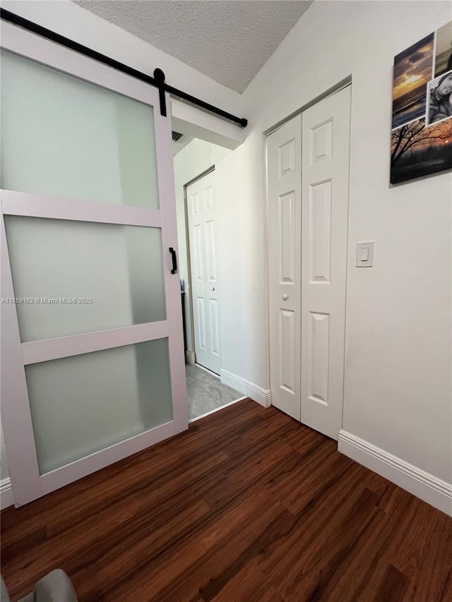 corridor featuring wood finished floors, a textured ceiling, baseboards, and a barn door