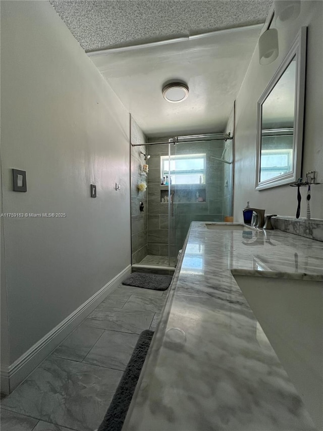 full bathroom with marble finish floor, a shower stall, baseboards, and a textured ceiling