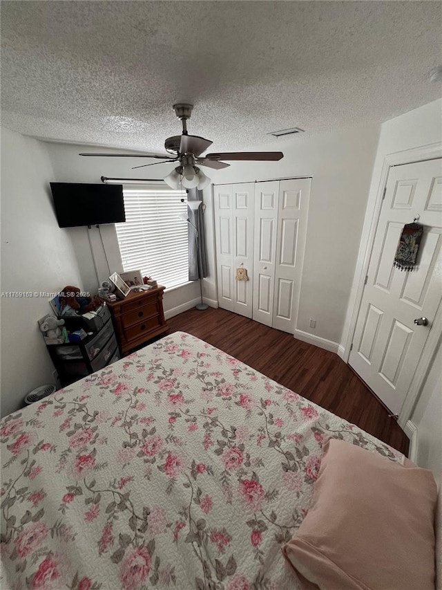 bedroom with a textured ceiling, dark wood-style flooring, baseboards, visible vents, and ceiling fan