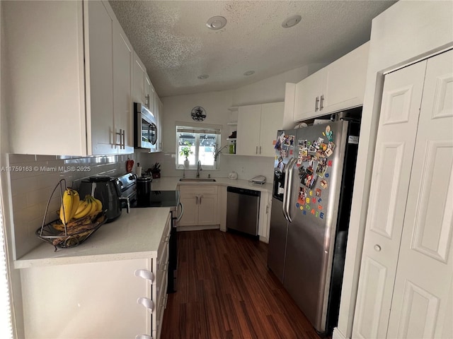 kitchen featuring lofted ceiling, light countertops, appliances with stainless steel finishes, white cabinets, and a sink