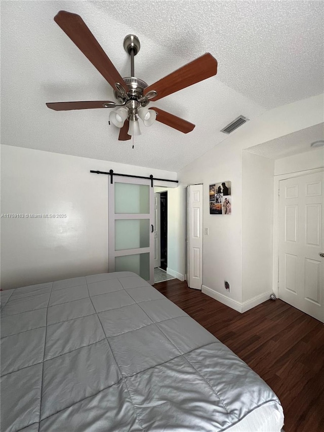 unfurnished bedroom with a barn door, visible vents, lofted ceiling, wood finished floors, and a textured ceiling