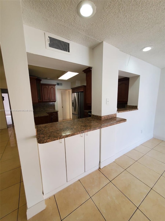 kitchen with light tile patterned floors, dark countertops, visible vents, and stainless steel fridge with ice dispenser