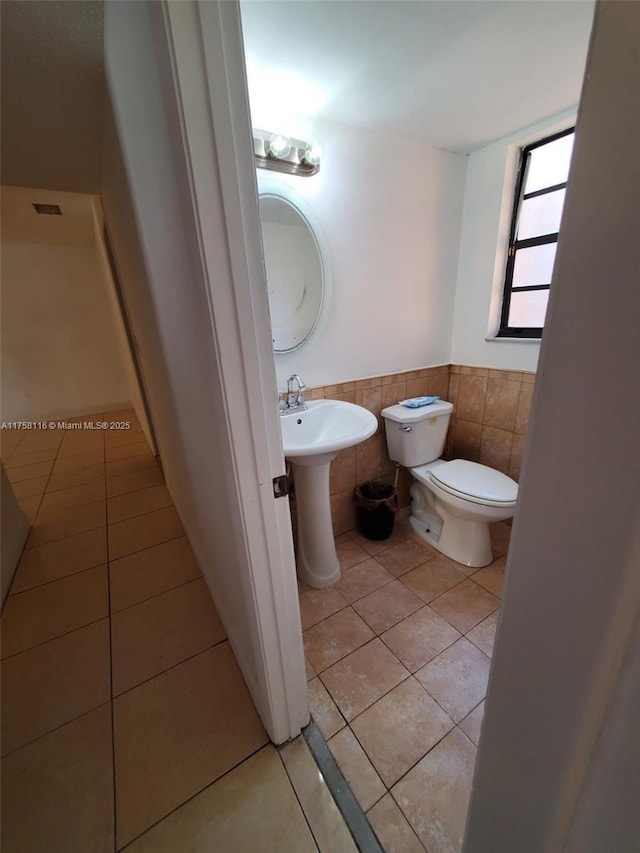 half bathroom with tile walls, toilet, a wainscoted wall, tile patterned floors, and a sink