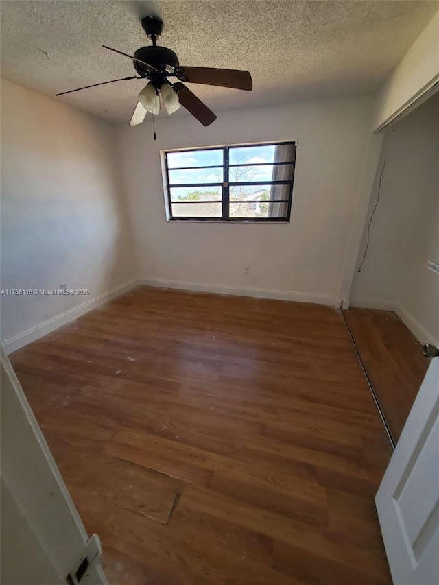 unfurnished room with a textured ceiling, wood finished floors, and baseboards