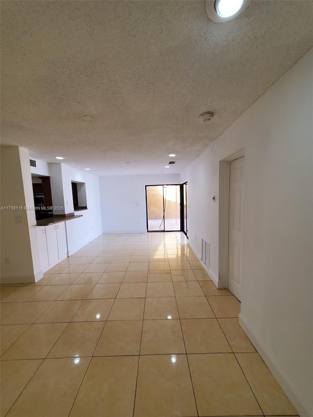 empty room with a textured ceiling, light tile patterned flooring, and baseboards