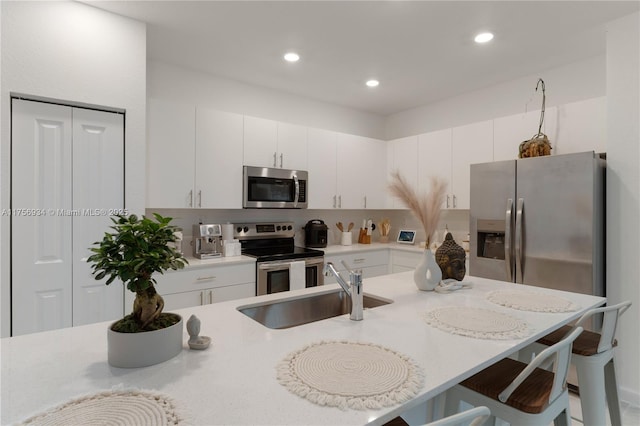 kitchen featuring stainless steel appliances, light countertops, white cabinets, a sink, and a kitchen breakfast bar