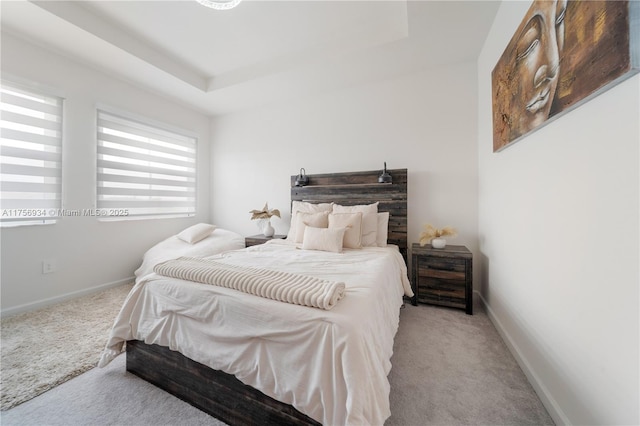 carpeted bedroom featuring baseboards and a tray ceiling