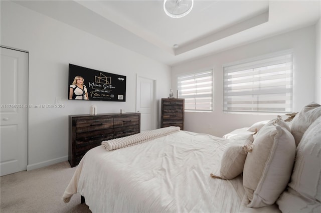 carpeted bedroom with a tray ceiling and baseboards