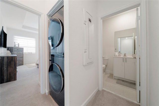 clothes washing area featuring stacked washing maching and dryer, baseboards, laundry area, and light colored carpet