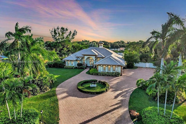 view of front of home with a yard, curved driveway, stucco siding, and fence