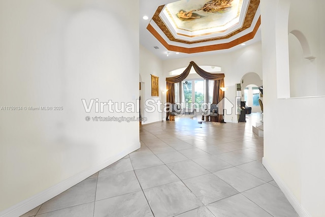 hall featuring a tray ceiling, arched walkways, baseboards, and light tile patterned flooring