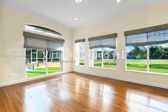 empty room with a healthy amount of sunlight, hardwood / wood-style floors, baseboards, and ornamental molding