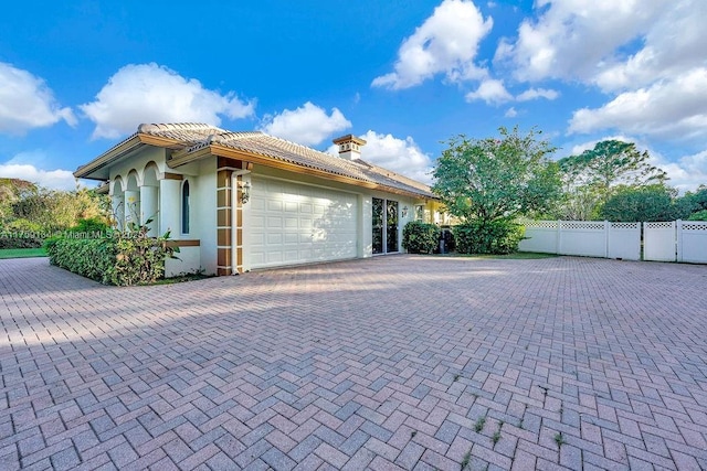 view of side of property featuring fence, a tile roof, stucco siding, decorative driveway, and a garage