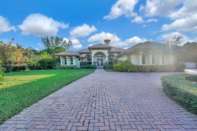 mediterranean / spanish home with a front lawn, a tiled roof, stucco siding, french doors, and decorative driveway