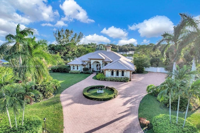 mediterranean / spanish-style home featuring stucco siding, fence, a front yard, and curved driveway