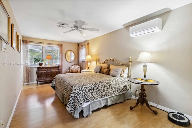 bedroom with a wall mounted air conditioner, wood finished floors, a ceiling fan, and baseboards