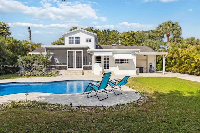 rear view of house featuring an outdoor pool, a lawn, a patio, a sunroom, and french doors