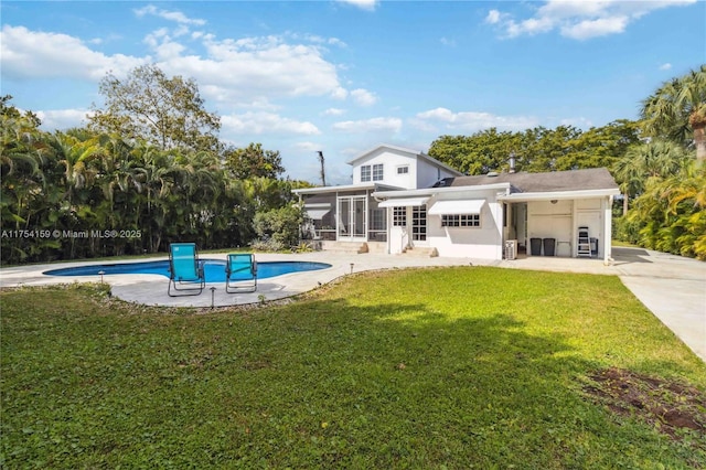 back of property featuring a sunroom, a patio area, an outdoor pool, and a yard