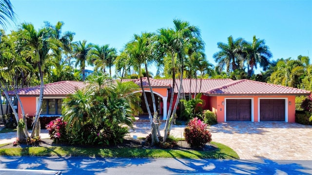 mediterranean / spanish home featuring stucco siding, a tiled roof, decorative driveway, and a garage