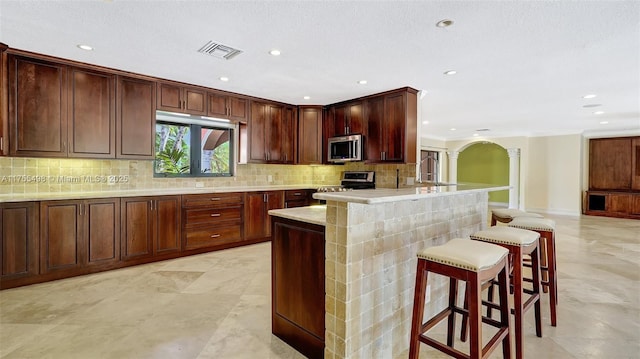 kitchen with visible vents, a breakfast bar, decorative columns, stainless steel appliances, and tasteful backsplash