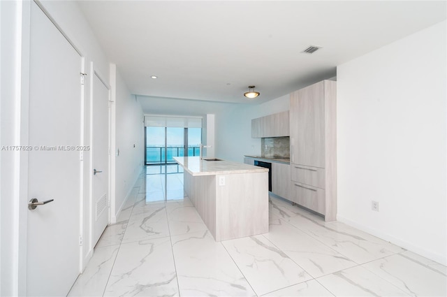 kitchen with marble finish floor, a center island with sink, visible vents, light brown cabinetry, and modern cabinets