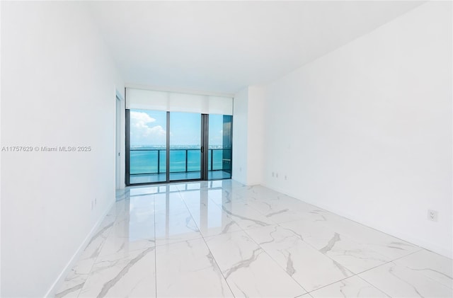 unfurnished room with marble finish floor, a wall of windows, and baseboards