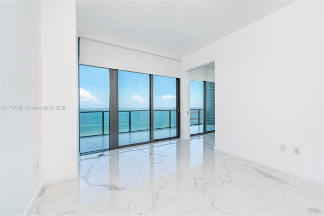 spare room with a water view, marble finish floor, and baseboards