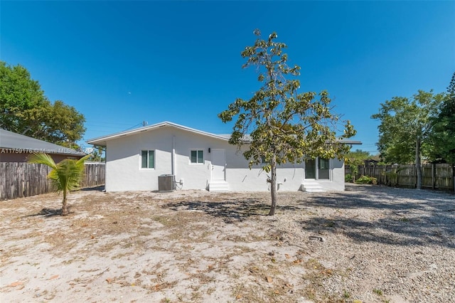 back of property with central AC, fence, and stucco siding