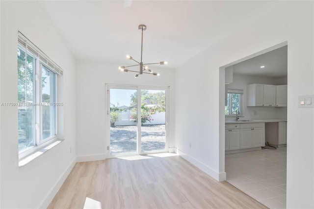 unfurnished dining area featuring light wood-style floors, plenty of natural light, an inviting chandelier, and baseboards