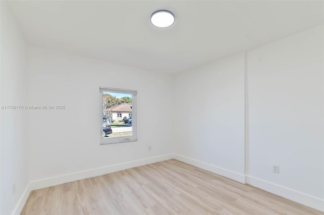 spare room with baseboards and light wood-style floors