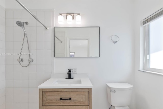 bathroom with toilet, a tile shower, and vanity