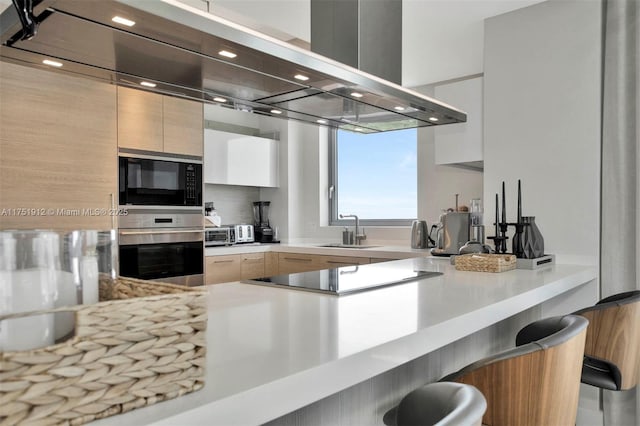 kitchen with light countertops, a sink, black appliances, island range hood, and a kitchen bar