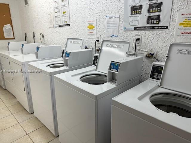 shared laundry area featuring a textured wall, washing machine and clothes dryer, and light tile patterned floors