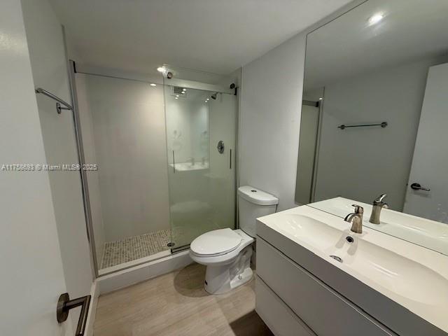 bathroom featuring vanity, wood finished floors, a shower stall, and toilet