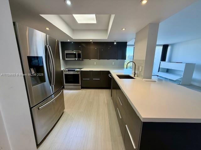 kitchen with a sink, light countertops, appliances with stainless steel finishes, a tray ceiling, and modern cabinets