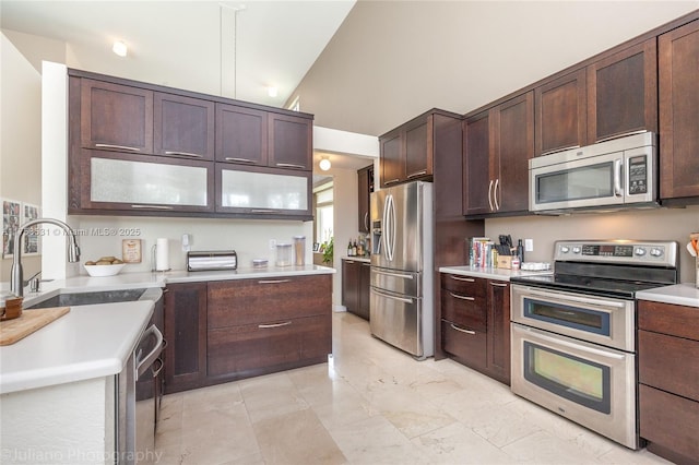 kitchen featuring stainless steel appliances, a sink, vaulted ceiling, dark brown cabinets, and light countertops