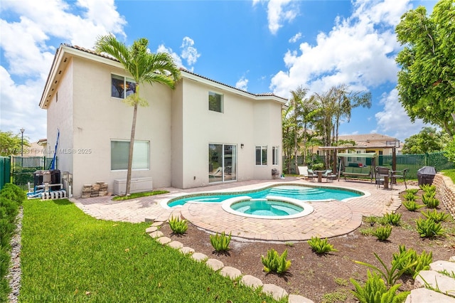 rear view of property featuring stucco siding, a pool with connected hot tub, fence, and a patio