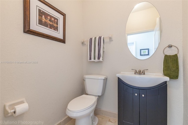 half bath with toilet, baseboards, and vanity