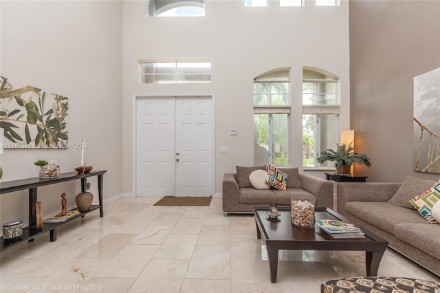 living area featuring marble finish floor, a high ceiling, and baseboards