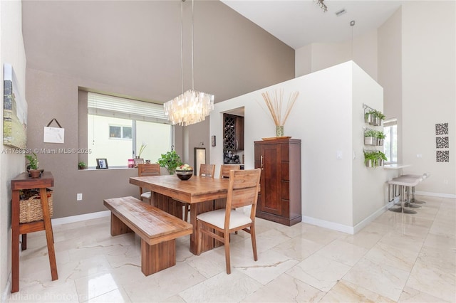 dining space featuring marble finish floor, a towering ceiling, and baseboards