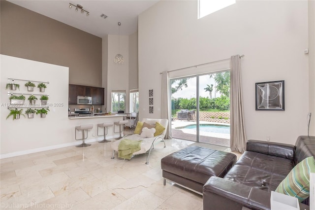 living area featuring a towering ceiling, baseboards, and a wealth of natural light