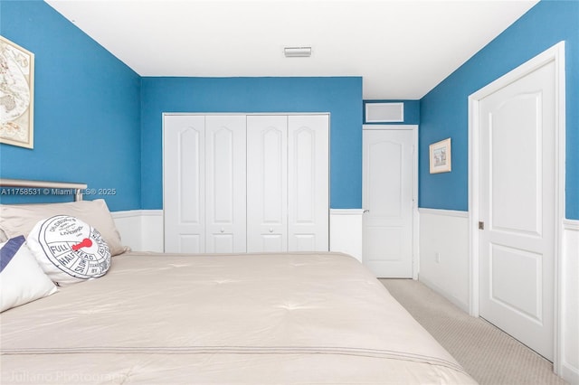 carpeted bedroom with a wainscoted wall, visible vents, and a closet