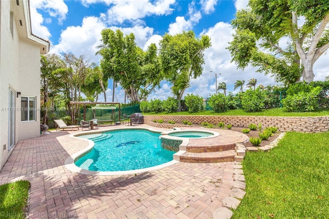 view of swimming pool featuring a yard, a pool with connected hot tub, fence, and a patio