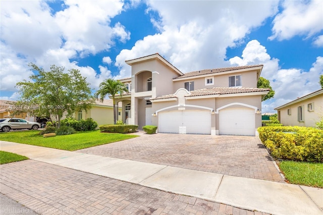 mediterranean / spanish house with decorative driveway, stucco siding, a front yard, a garage, and a tiled roof