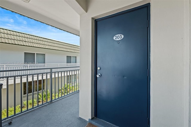 doorway to property with a balcony, a tiled roof, and stucco siding