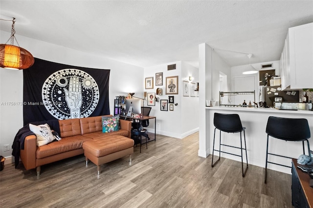 living room with a textured ceiling, light wood finished floors, visible vents, and baseboards